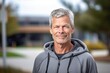Headshot portrait photography of a satisfied mature man wearing a comfortable hoodie against a school campus background. With generative AI technology