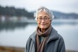 © Markus Schröder - Environmental portrait photography of a grinning old woman wearing a cozy sweater against a scenic lagoon background. With generative AI technology