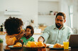 © Zamrznuti tonovi - An african american mother is feeding her son while sitting with her working father at the breakfast table at home in the morning.