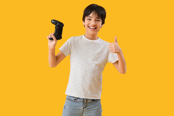 Wall Mural - Little boy with game pad showing thumb-up on yellow background
