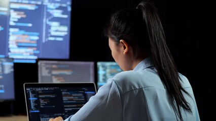Close Up Back View Of Asian Female Programmer Having A Headache While Writing Code By A Laptop Using Multiple Monitors Showing Database On Terminal Window Desktops In The Office
