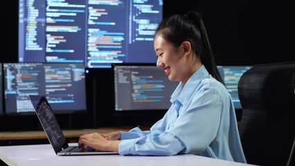Side View Of Asian Female Programmer Writing Code By A Laptop Using Multiple Monitors Showing Database On Terminal Window Desktops In The Office
