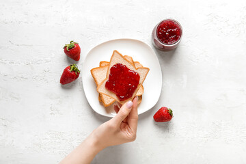 Woman holding tasty toast with strawberry jam on grunge white background