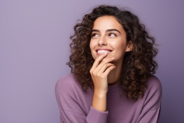 Medium shot portrait photography of a grinning girl in her 20s putting the hand on the chin as if thinking against a lilac purple background. With generative AI technology