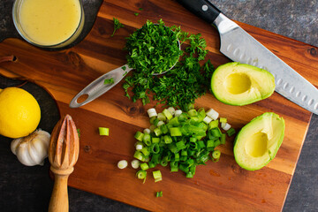 Wall Mural - Prepping Scallions, Parsley, and Avocado for a Healthy Salad: Chopped vegetables on a wooden cutting board with a santoku chef's knife