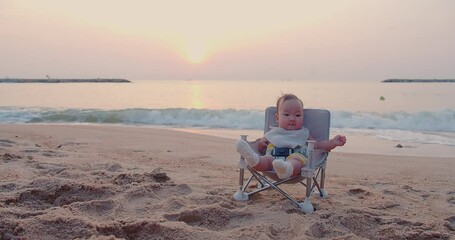 Wall Mural - happy cute adorable little baby infant smiling carefree relaxing sitting on outdoor chair at nature ocean sea beach during beautiful sunrise sunset sky in summer holiday enjoy leisure vacation travel