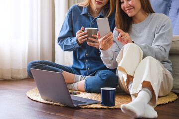 Wall Mural - Closeup image of a young couple women using mobile phone and laptop computer together