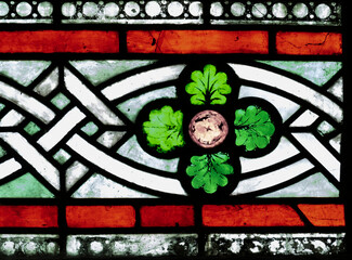 Close up of stained glass panel in a church showing celtic knot work, four green leaves and a red border