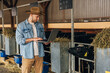 © cherryandbees - A farmer is standing in a stable and using laptop.