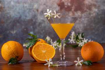 Wall Mural - A glass decorated with white flowers contains orange juice, with whole and halved oranges next to it