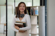 © Songsak C - Portrait of an attractive pretty young Asian female college student standing in a campus library. Education concept.