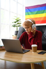 Focused young Asian gay man student in headphone looking at laptop screen watching tutorial, lecture or studying online at home