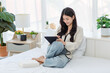 © Bangkok Click Studio - Asian young cheerful female teenage model sitting smiling on white clean sheet bed using pen with touchscreen tablet computer browsing surfing internet shopping working online in modern decor bedroom