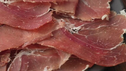 Poster - plate of sliced spanish iberico ham on wooden table background, rotating