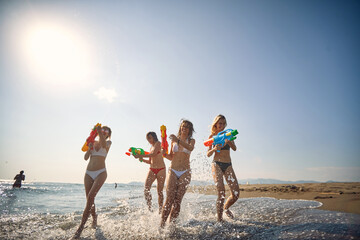 Friends having fun on the beach.Playful girl have fun with water gun at beach at sunny day.