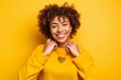 Headshot portrait photography of a grinning girl in her 20s making a heart with the hands against a bright yellow background. With generative AI technology