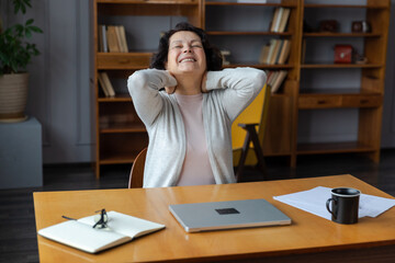 Wall Mural - Middle aged senior woman at home relaxing stretching hands and body taking break from work on laptop. Older mature woman happy after work done satisfied by good result. Fatigue from long laptop usage