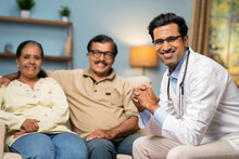 Happy Smiling Indian Family Doctor With Senior Couple Looking At Camera During Home Visit - Concept Of Healthcare Service, Medical Treatment And Home Consultation.