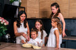 © dvulikaia - Young mother cooking sweet cheesecake with four her daughters at home.