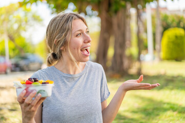 Wall Mural - Young blonde woman holding a bowl of fruit at outdoors with surprise facial expression