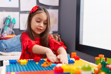 Wall Mural - Adorable hispanic girl playing with construction blocks sitting on table at kindergarten