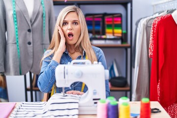 Wall Mural - Blonde woman dressmaker designer using sew machine afraid and shocked, surprise and amazed expression with hands on face