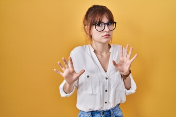 Poster - Young beautiful woman wearing casual shirt over yellow background moving away hands palms showing refusal and denial with afraid and disgusting expression. stop and forbidden.