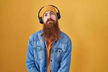 Wall Mural - Caucasian man with long beard listening to music using headphones looking sleepy and tired, exhausted for fatigue and hangover, lazy eyes in the morning.