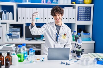 Poster - Young hispanic man scientist using laptop measuring liquid at laboratory