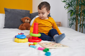 Adorable hispanic boy playing with hoops game sitting on bed at bedroom