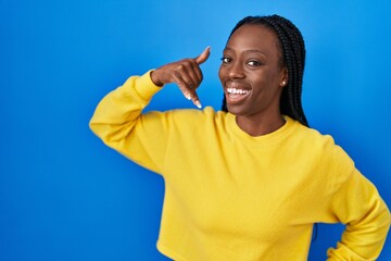 Wall Mural - Beautiful black woman standing over blue background smiling doing phone gesture with hand and fingers like talking on the telephone. communicating concepts.