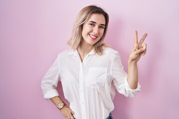 Poster - Young beautiful woman standing over pink background smiling looking to the camera showing fingers doing victory sign. number two.