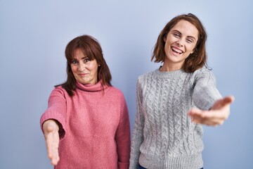 Sticker - Mother and daughter standing over blue background smiling friendly offering handshake as greeting and welcoming. successful business.