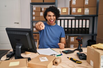 Wall Mural - Hispanic man with curly hair working at small business ecommerce pointing displeased and frustrated to the camera, angry and furious with you