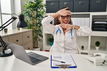 Sticker - Young hispanic woman wearing doctor uniform and stethoscope smiling cheerful playing peek a boo with hands showing face. surprised and exited