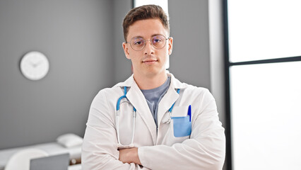 Wall Mural - Young hispanic man doctor standing with serious expression and arms crossed gesture at clinic