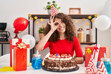 Sticker - Hispanic woman with curly hair celebrating birthday holding big chocolate cake smiling happy doing ok sign with hand on eye looking through fingers