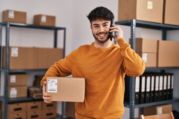 Wall Mural - Young hispanic man ecommerce business worker talking on smartphone holding package at office