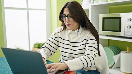 Wall Mural - Young beautiful hispanic woman using laptop with serious expression at dinning room