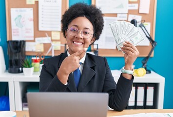 Canvas Print - Beautiful african woman with curly hair holding money at the office smiling happy pointing with hand and finger