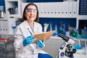 Sticker - Middle age woman scientist smiling confident reading book at laboratory