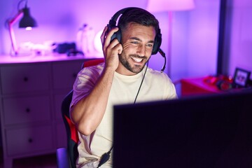 Young hispanic man streamer smiling confident sitting on table at gaming room