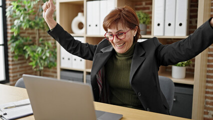 Mature hispanic woman business worker using laptop celebrating at office