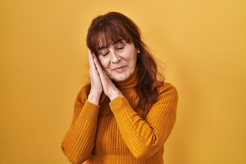 Canvas Print - Middle age hispanic woman standing over yellow background sleeping tired dreaming and posing with hands together while smiling with closed eyes.