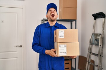 Wall Mural - Young hispanic man working on moving service holding boxes angry and mad screaming frustrated and furious, shouting with anger looking up.