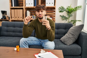 Canvas Print - Arab man with beard working on depression holding pills and water skeptic and nervous, frowning upset because of problem. negative person.