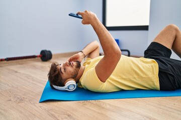 Poster - Young arab man listening to music lying on yoga mat at sport center