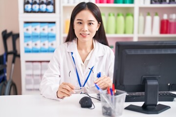 Sticker - Young chinese woman pharmacist smiling confident holding glasses at pharmacy