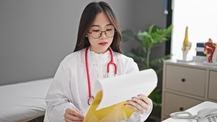 Canvas Print - Young chinese woman doctor reading document on clipboard at clinic