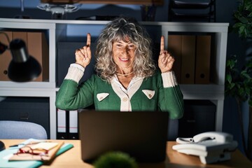 Sticker - Middle age woman working at night using computer laptop smiling amazed and surprised and pointing up with fingers and raised arms.